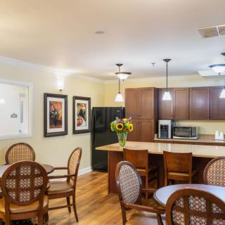 A cozy kitchen and dining area featuring a breakfast bar with bar stools, wooden tables and chairs, and warm lighting.