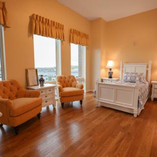 A cozy bedroom with a warm orange color scheme featuring wooden flooring, elegant armchairs, and a white bed.