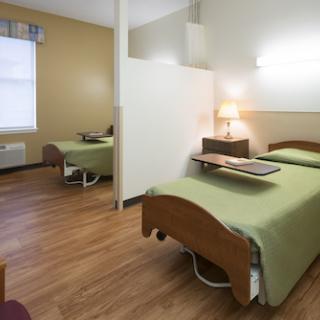 A bright and tidy hospital room featuring two beds with green linens, designed for patient comfort.