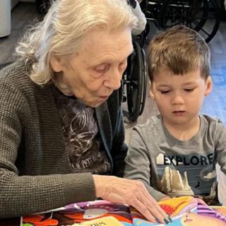 An elderly person and a young child are reading a book together, highlighting intergenerational interaction.