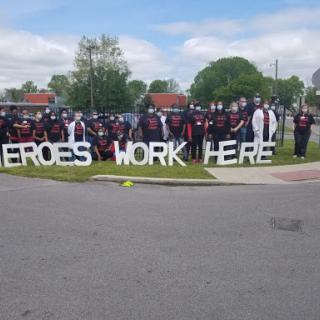 A gathering of dedicated individuals proudly showcasing their commitment with a sign that reads 'Heroes Work Here'.
