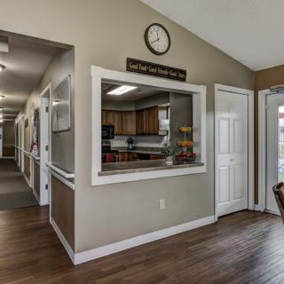 A view of a kitchen and corridor area with a reception window and clock on the wall.