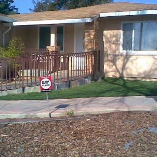 A suburban house with a front yard, featuring a 'For Sale' sign on the lawn.