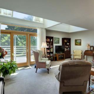A cozy living room with ample natural light, featuring comfortable seating and a bookshelf.