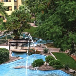A scenic garden landscape featuring a small bridge over a water stream, surrounded by lush greenery and trees.