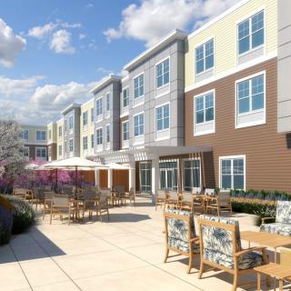 A modern apartment complex featuring outdoor patio seating under a clear blue sky.