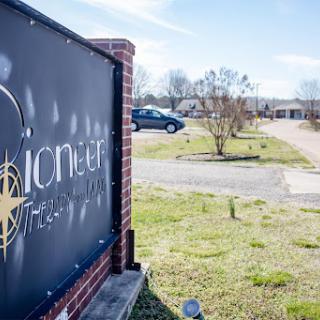 A view of the Pioneer sign in an open area with a building and parked car in the background.