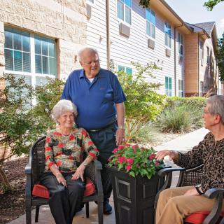 A group of seniors enjoying a conversation outside in a garden setting.