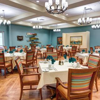 A well-decorated dining room featuring elegantly set tables, wooden chairs with colorful cushions, and chandeliers overhead.
