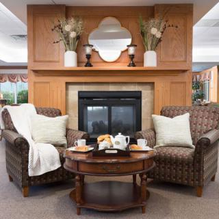A cozy living room with two armchairs facing a fireplace, adorned by a decorative mirror and vases with plants on the mantel.