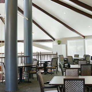 A spacious restaurant interior with tables and chairs arranged neatly under a high ceiling with visible beams.