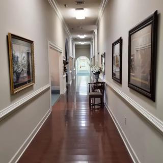 A long hallway featuring wooden flooring and adorned with framed paintings on the walls.