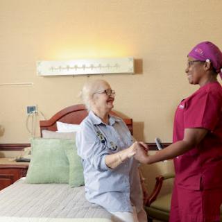 A nurse provides care and support to an elderly patient in a hospital room.
