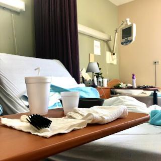 A view of a hospital room showing a bed, food and drink on the tray, and medical equipment in the background.