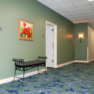 A hallway with a bench, painting, and door, featuring patterned carpet and wall sconces.