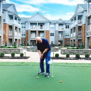 A person practicing putting on a green in front of an apartment complex.
