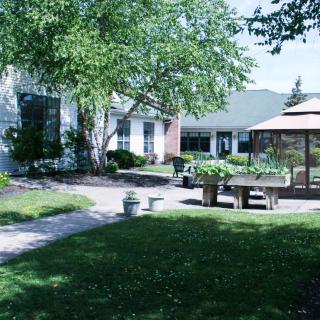 A serene garden with a gazebo, benches, and a pathway surrounded by lush trees and landscaping.