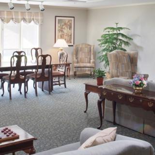 A well-furnished living room with a dining area, featuring elegant chairs, a large window, and decorative elements such as artwork and a potted plant.