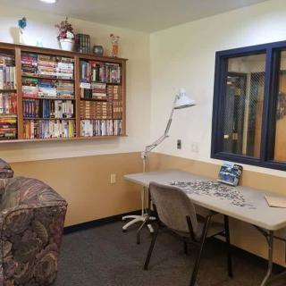A cozy library corner featuring a bookshelf filled with books, a desk with a lamp, and comfortable seating.