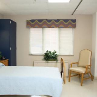 A neatly arranged bedroom with a bed, chair, and window featuring a plant on the sill.