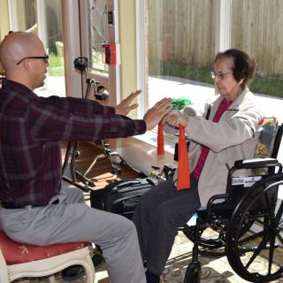 A caregiver assists an elderly person in a wheelchair with physical therapy exercises using resistance bands.