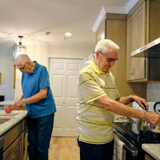 Two elderly men preparing food in a kitchen together.