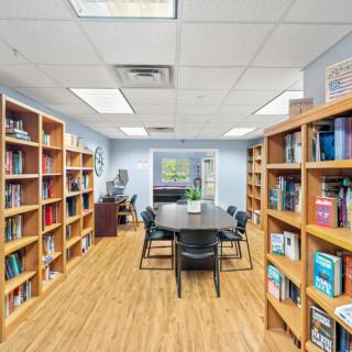 A cozy library study room with bookshelves lining the walls and a central meeting table surrounded by chairs.