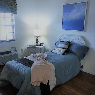 A cozy bedroom with a neatly made bed, featuring pillows and a throw blanket, illuminated by a lamp on the nightstand.