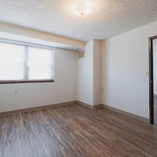 A spacious, empty room with natural light coming in through the window and a door leading to another area.