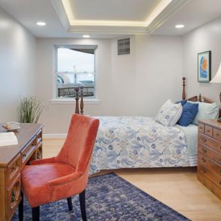 A cozy bedroom featuring a wooden desk and chair, a neatly made bed with floral bedding, and soft lighting.