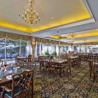 A spacious and elegantly decorated restaurant dining room with chandeliers, carpeted flooring, and large windows.