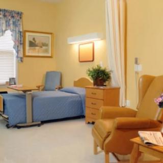 A neatly arranged hospital room with a bed, chairs, and natural lighting.