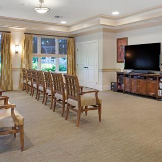 A well-lit meeting room with rows of wooden chairs facing a large television.