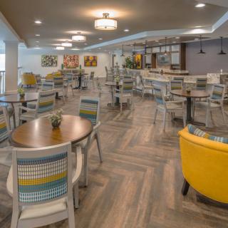 A modern restaurant with colorful chairs and a bar area.