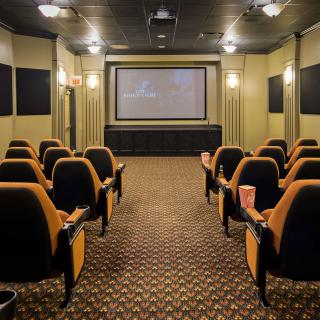 An empty theater room with rows of seats facing a large screen.