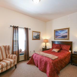 A cozy bedroom with a red bedspread, side tables, and framed artwork on the walls.