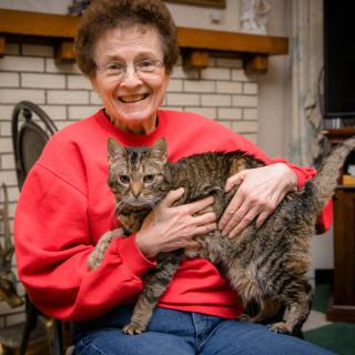 An elderly woman smiling and holding her cat indoors.