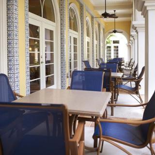 A covered outdoor patio with tables and chairs set along a corridor with arched architecture.