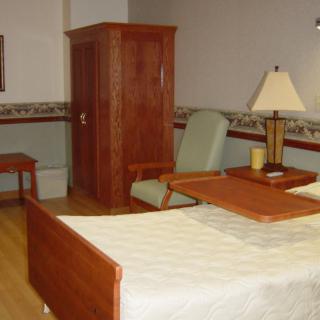 A hospital room with a bed, chair, and wooden furniture.