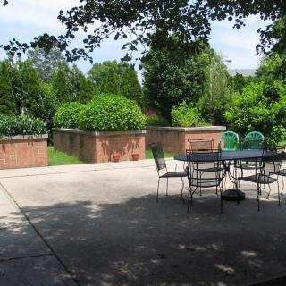A tranquil patio area with outdoor seating surrounded by lush greenery on a sunny day.