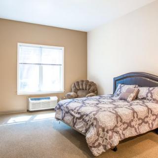 A cozy bedroom with a bed, chair, and a window letting in natural light.
