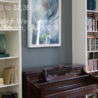 A cozy corner in a living room featuring a piano, bookshelf, and artwork.