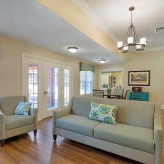 A cozy living room with a sofa and armchair, featuring a chandelier and wood flooring.