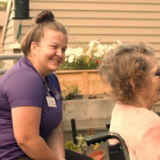 A caregiver shares a joyful moment with an elderly woman in a garden setting.