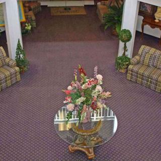 A cozy lobby area featuring a glass table with a floral arrangement, surrounded by patterned sofas and decorative plants.