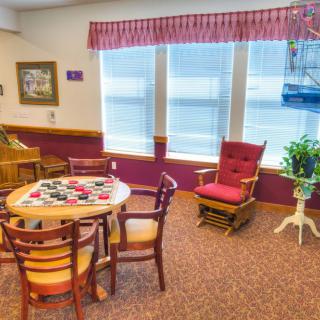 A cozy room with a round table, chairs, and a red armchair near a window.
