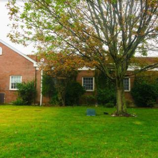 A peaceful exterior view of a brick house surrounded by a lush lawn and a tree.