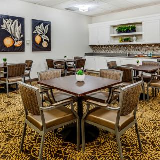 A spacious dining area with arranged tables and chairs, featuring decorative artwork and a carpeted floor.