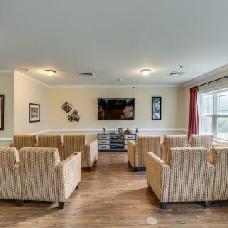 A cozy seating area with multiple chairs facing a television, featuring wooden flooring and large windows.