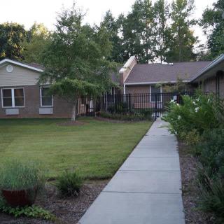 A serene pathway leading to a house surrounded by a well-maintained garden and trees.